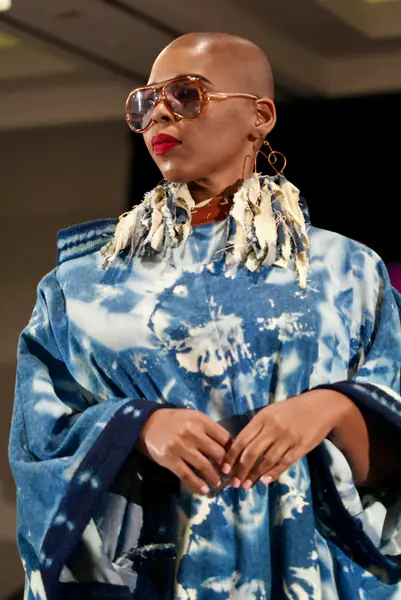 A model wears oversized sunglasses, large heart-shaped earrings and a blue tie-dye poncho with fringe.