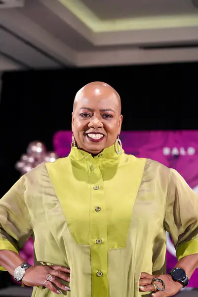 A smiling bald model wears a high-collared chartreuse shirt.