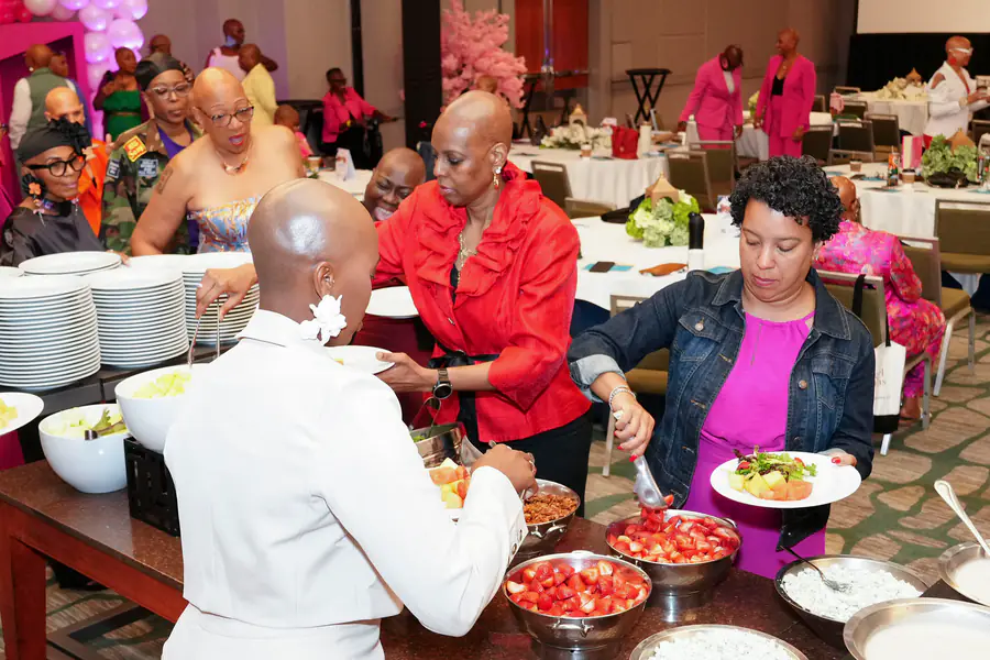 Several bald people serve themselves food from a buffet line at a conference celebrating baldness and hair loss.