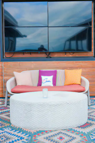 A white circular coffee table sits in front of a sofa with a white pillow that reads Baldie Con.